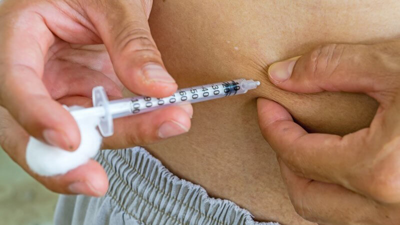 Diabetiker in grauen Shorts gibt sich eine Insulinspritze in den Bauch