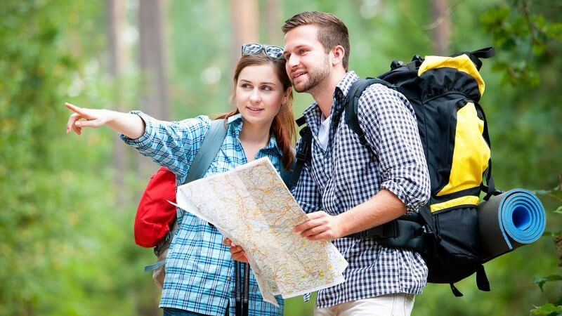 Paar beim Wandern in Wald mit Rucksäcken und Karte