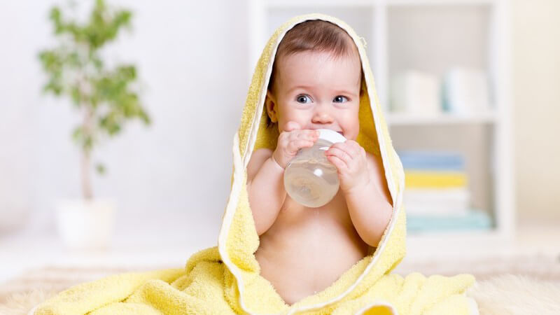 In gelbes Handtuch gewickeltes Baby trinkt aus einem Fläschchen