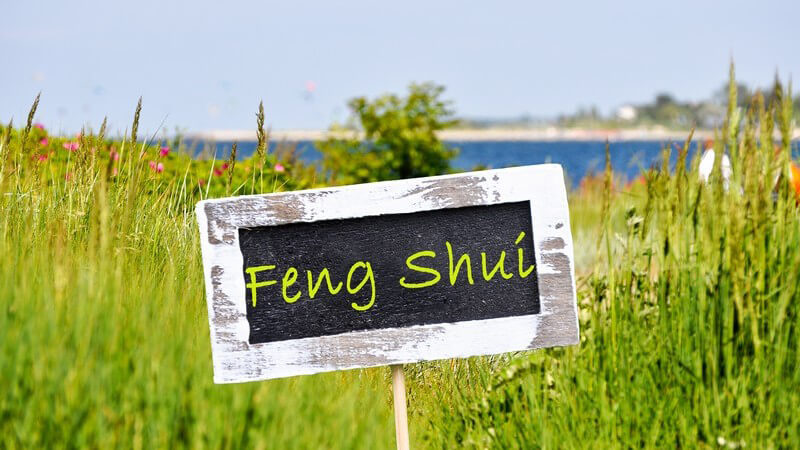 Holzschild mit der Aufschrift "Feng Shui" steht auf einer Wiese an einem See