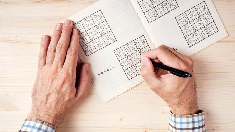 Mann in kariertem Hemd beim Sudoku spielen auf einem hellen Holztisch