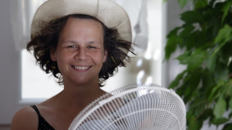 Lachende Frau mit Strohhut vor weißem Ventilator, Haare zurückgeweht