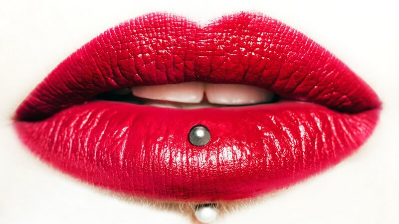 Nahaufnahme von knallrot geschminkten Lippen mit Labret-Piercing (Lippenpiercing)