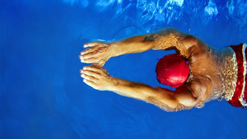 Schwimmer mit roter Badekappe und roter Schwimmshort von oben, die Arme nach vorne gestreckt
