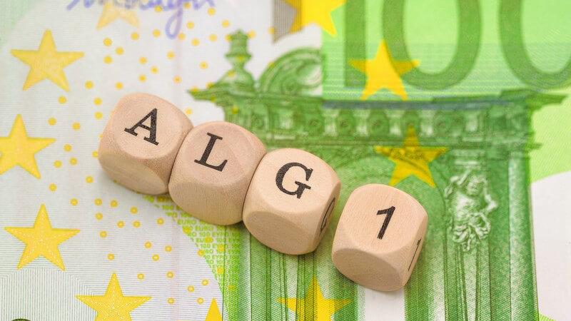 Buchstabenwürfel aus Holz bilden das Wort "ALG1" auf einem grünen 100-Euro-Geldschein