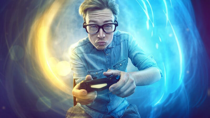 Junger Mann mit Jeanshemd und Nerdbrille beim Zocken am Gamecontroller, abstrakter Hintergrund