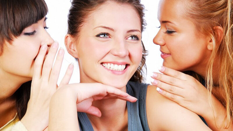Zwei Frauen flüstern ihrer Freundin etwas ins Ohr