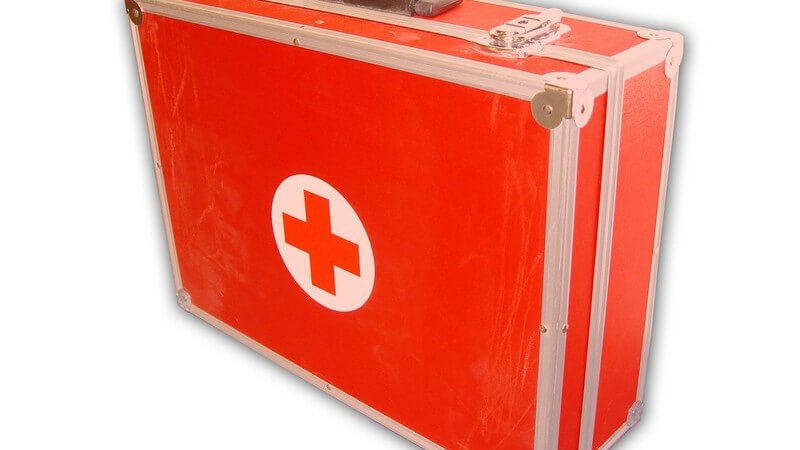 Arztkoffer, Notfallkoffer, leuchtend roter Kastenkoffer mit rotem Kreuz, vor weißem Hintergrund