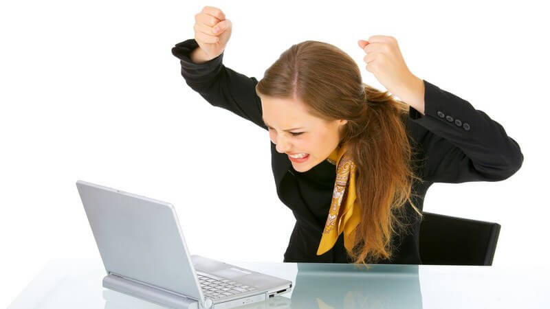 Geschäftsfrau sitzt am Laptop und hält frustriert die Fäuste in die Luft