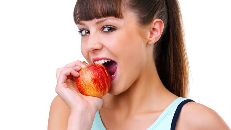Junge Frau im Sportoutfit beisst in roten Apfel