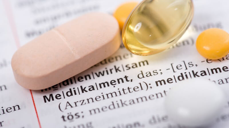 Mehrere Tabletten und Pillen liegen auf Wörterbuch auf Begriff Medikament