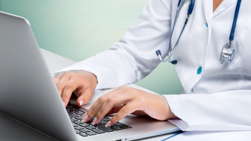 Ärztin in weißem Kittel und Stethoskop um den Hals tippt auf einem Laptop