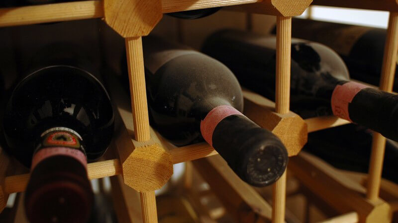 Nahaufnahme Weinregal aus Holz mit verstaubten Rotweinflaschen