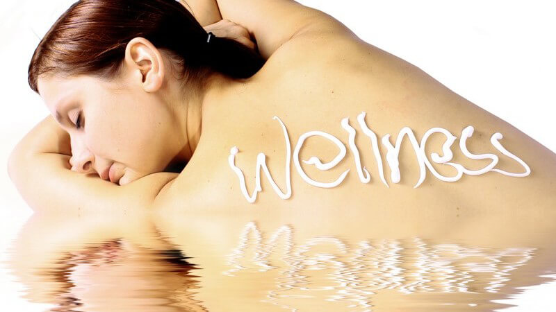 Junge Frau entspannt an Wasser, hat mit Creme "Wellness" auf Rücken geschrieben
