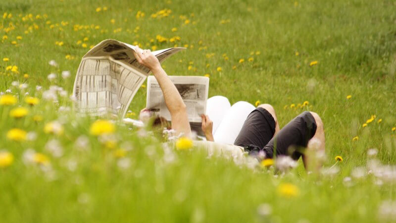 Junges Paar liegt auf Wiese und liest Zeitung