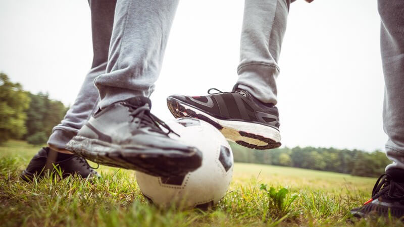 Beine zweier Jungen beim Fußballspielen auf einer Wiese