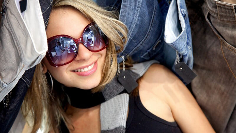 Blonde Frau mit Sonnenbrille zwischen Jeans im Geschäft
