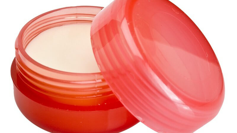 Rotes Kosmetikdöschen mit Lippenbalsam vor weißem Hintergrund