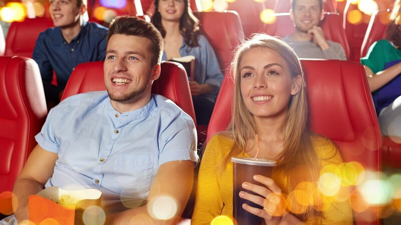 Junge Kinozuschauer mit Popcorn und Getränken in roten Sitzen