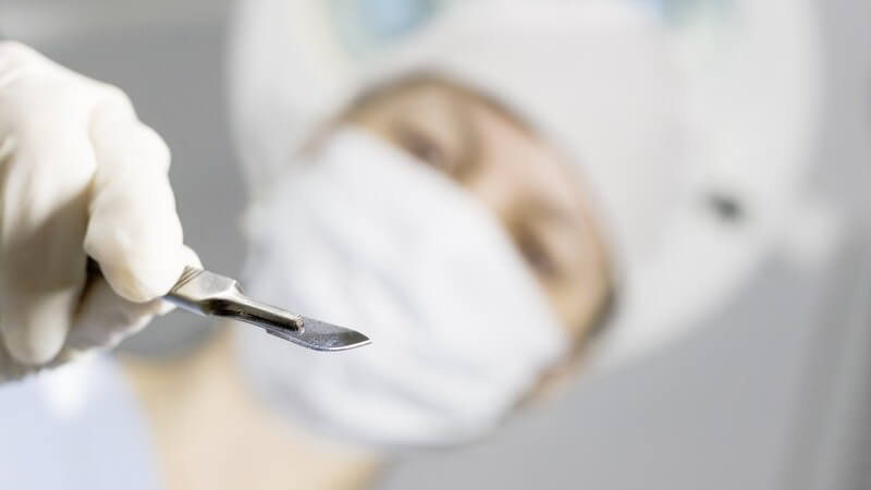 Von unten: Ärztin mit Kopfhaube und Mundschutz, hält Skalpell in rechter Hand, setzt an ,Operation, Chirurgie, Schnitt
