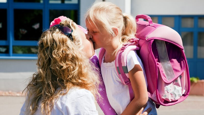 Mutter gibt kleiner Tochter Kuss am ersten Schultag