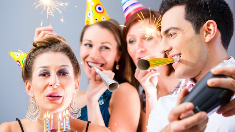 Vier Freunde feiern Geburtstag mit Partyhüten, Tröten und Geburtstagskuchen