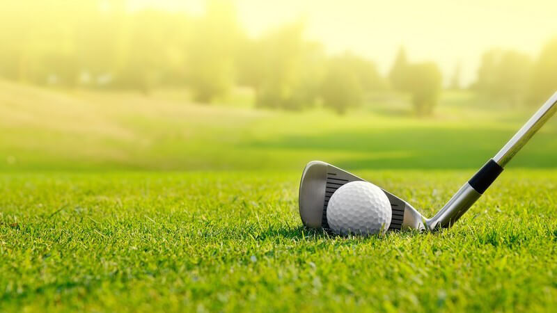 Golfschläger und Golfball auf dem Rasen eines Golfplatzes im Sonnenlicht