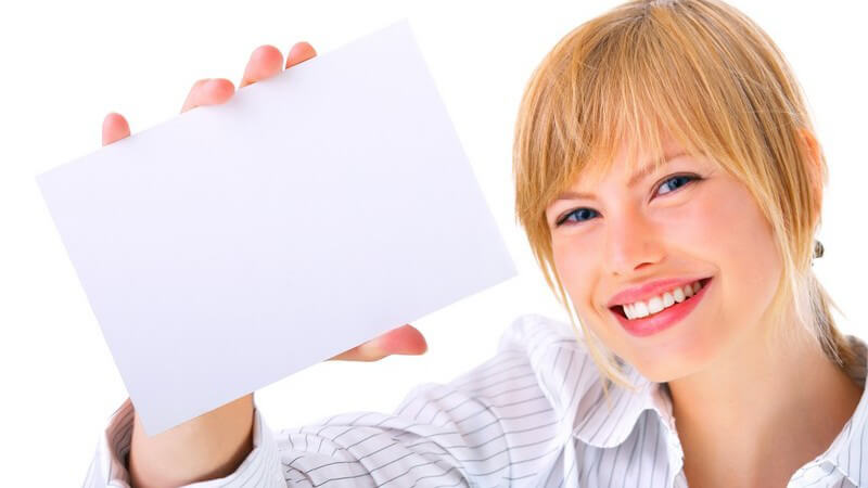 Blonde, lächelnde Frau hält leeren, weißen Briefumschlag in Kamera