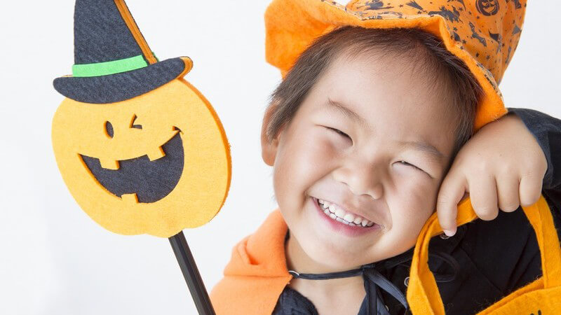 Lächelndes, asiatisches Kind im orangen Hexenkostüm zu Halloween