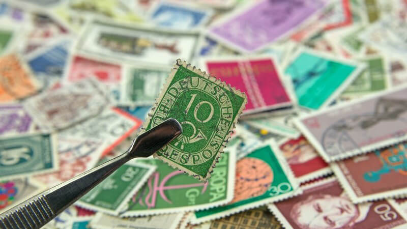 Pinzette mit grüner Briefmarke, im Hintergrund eine Briefmarkensammlung