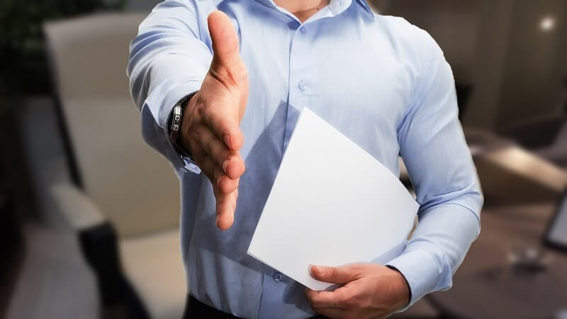 Geschäftsmann in blauem Hemd und mit Papier in der Hand reicht die andere Hand zur Begrüßung