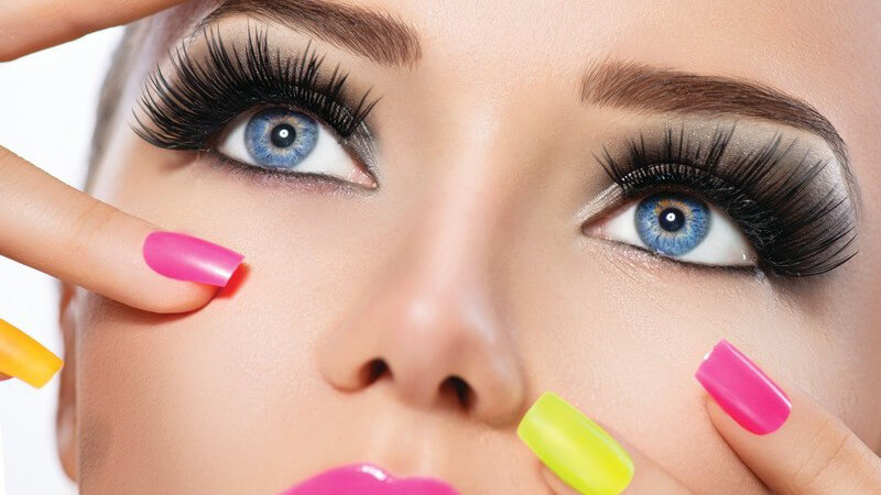 Geschminktes Modelgesicht mit pinkem Lippenstift und pinken und gelben Fingernägeln