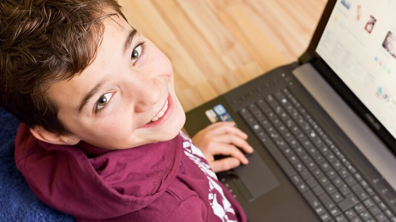 Junge mit Notebook oder Laptop auf dem Schoß surft im Internet