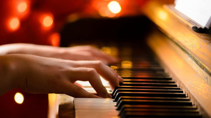 Hände spielen auf einem Klavier, Lichter im Hintergrund