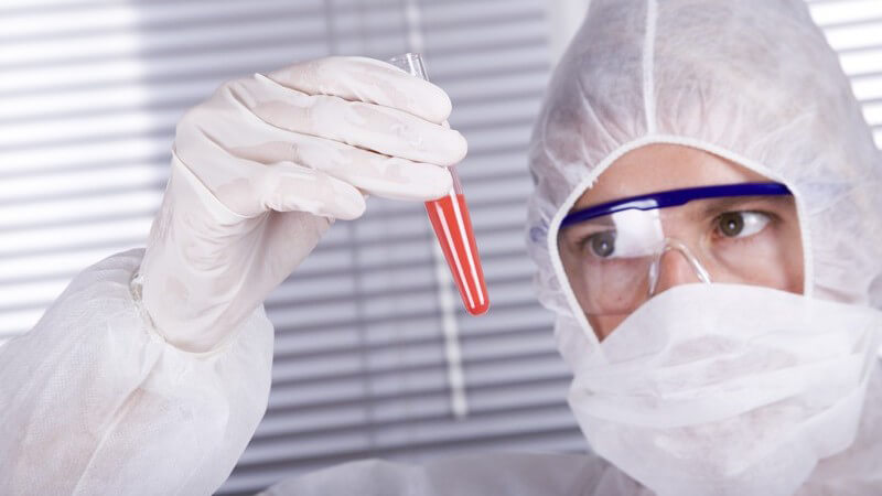 Laborarzt mit Schutzkleidung analysiert eine Blutprobe im Reagenzglas