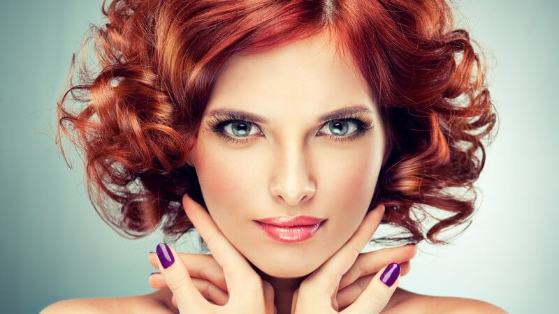 Model mit Make-up, lila Fingernägeln und roten Locken