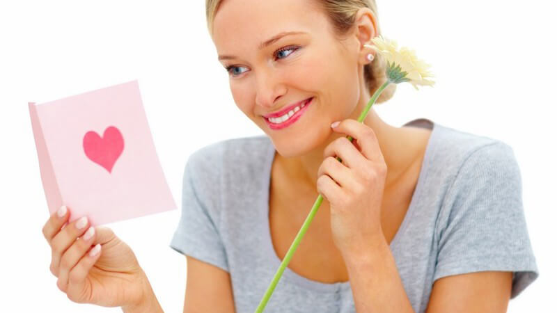 Frau hält Blume in Hand und schaut sich Valentinskarte an