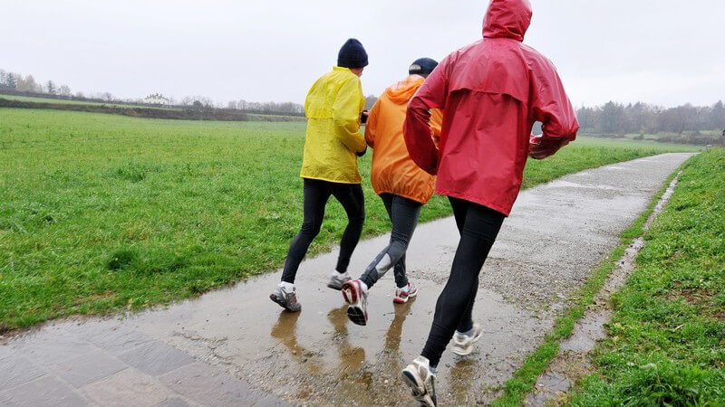 Rückansicht drei Sportler beim Joggen im Regen mit Regenjacken