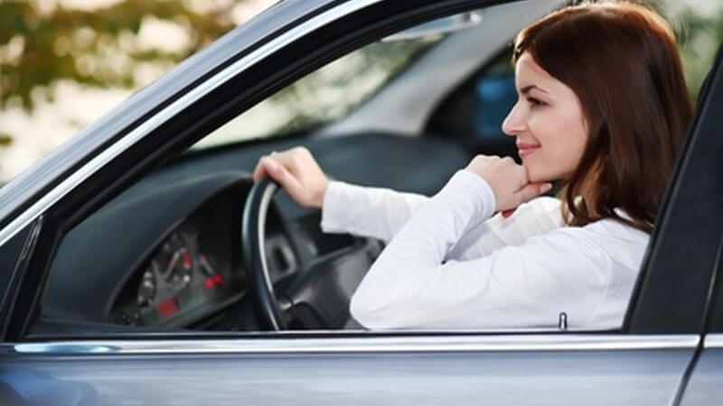 Verkehr - Junge Frau sitzt gelassen am Steuer ihres Autos