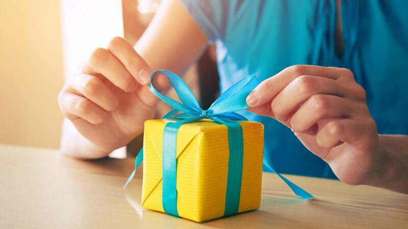 Frau bindet eine blaue Schleife an eine kleine gelbe Geschenkbox