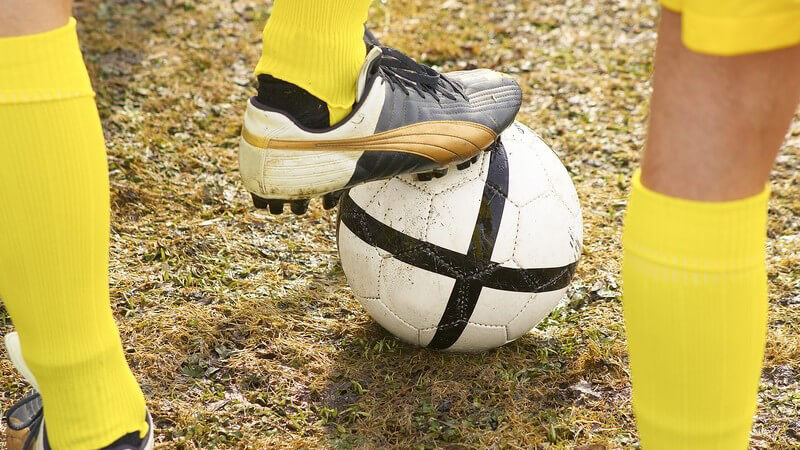 Beine von Fußballern in gelben Trikots mit Fußball