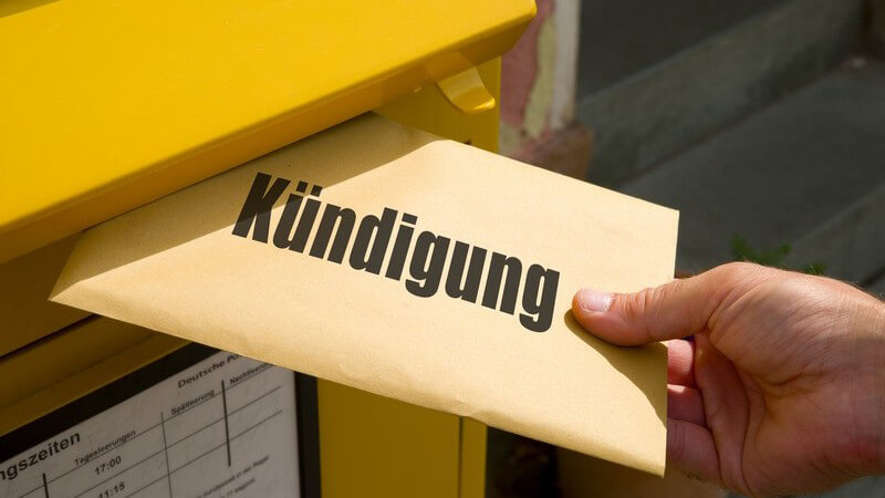 Hand wirft einen Brief mit der großen Aufschrift "Kündigung" in einen gelben Post-Briefkasten