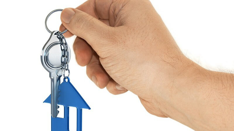 Männliche Hand hält Schlüssel mit Haus-Schlüsselanhänger hoch