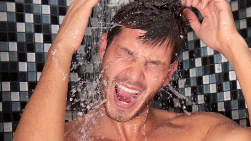 Mann mit offenem Mund und hochgehobenen Armen unter der Dusche