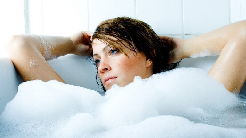 Junge, nachdenkliche Frau in Badewanne mit viel Schaum