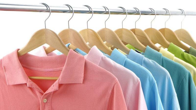 Neun farbige Poloshirts hängen mit Bügel an Kleiderstange