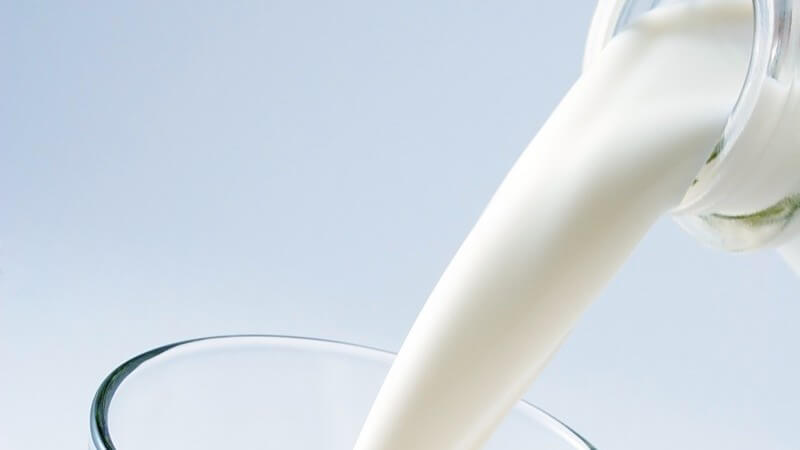Nahaufnahme Milch aus Glasflasche wird in ein Glas gekippt