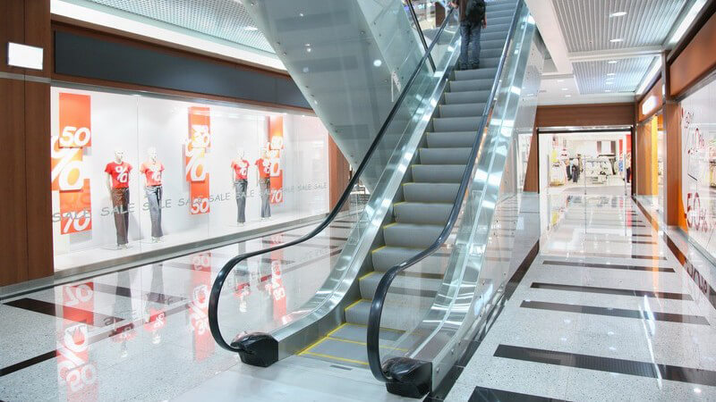 Mann fährt auf Rolltreppe nach oben in großem Einkaufscenter