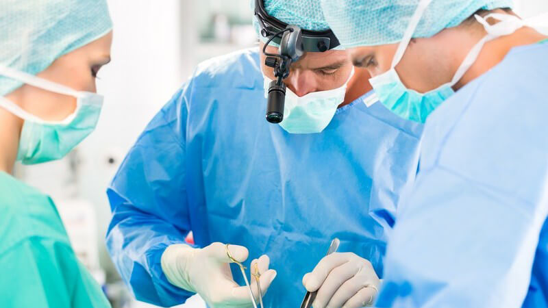 Chirurgen-Team in blau und grün während einer Operation, ein Chirurg trägt eine Lampe am Kopf