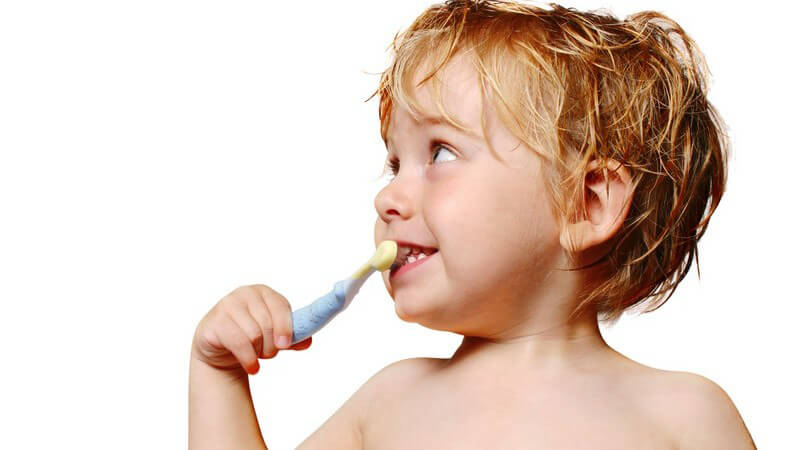 Kleiner Junge mit nassen Haaren hält Zahnbürste in Mund, schaut zur Seite